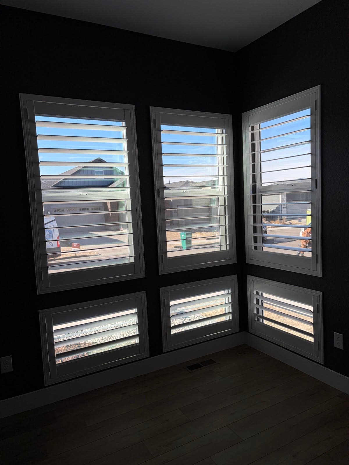 Plantation shutters wrapping a corner of six windows in a charcoal-walled room