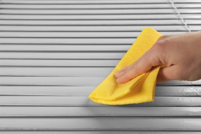 A person cleaning blinds with a yellow cloth